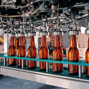 Bouteilles en verre en mouvement dans une usine de fabrication de boissons. La surveillance de la dureté de l'eau est importante pour garantir une qualité optimale des produits.