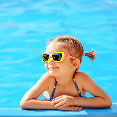 Enfant souriant au bord d'une piscine. Dans les piscines, la dureté de l'eau peut endommager la surface des bassins et corroder les tuyaux.